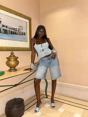 Adut Akech wears long denim shorts, a sheer white top, sparkly silver shawl, and Prada heels