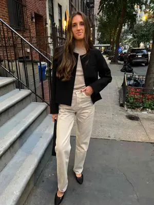 Stylist Jordanna Sharp wears a neutral sweater, off-white trousers, a black jacket, and flats
