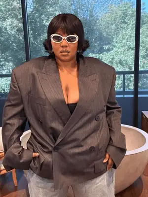 Lizzo wears an oversized double-breasted blazer, trousers, and white sunglasses