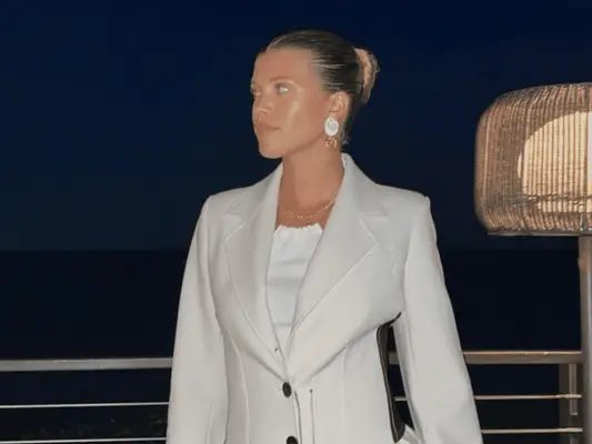 Sofia Richie Grainge wears a gray blazer, high neck top, and oversized earrings