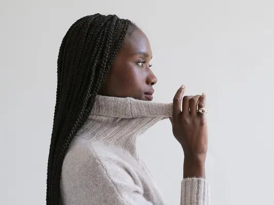 Side profile photo of woman wearing gray turtleneck sweater and gold pinky ring