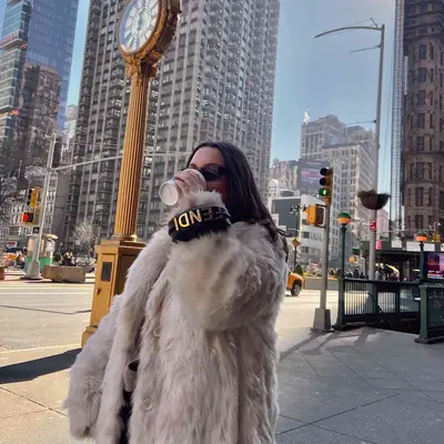 MYM Beauty writer Bella Gerard sips coffee while wearing a Fendi bracelet bag and white fur coat