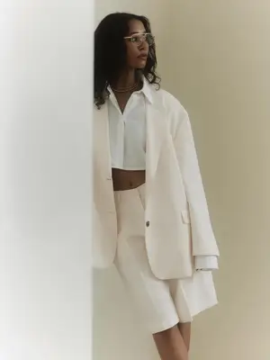 Woman wears white button-down shirt, blazer, and trousers and aviator glasses