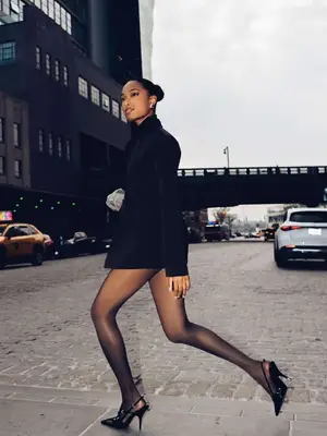 Woman walking while wearing black blazer dress, sheer black tights, and slingback heels