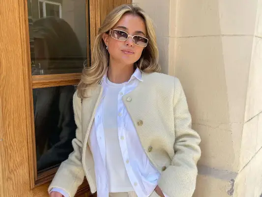 Matilda Djerf wears a white t-shirt, button-down, cream sweater, and sunglasses