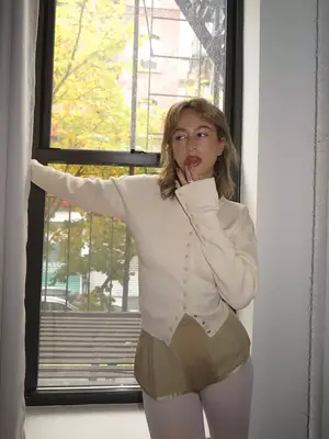 TikTok star Izzi wears a cream-colored button-down cardigan, tan mini shorts, and white tights