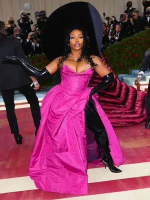 SZA wearing a pink Vivienne Westwood dress, black latex opera gloves, black tall boots, and oversized hat to the 2022 Met Gala