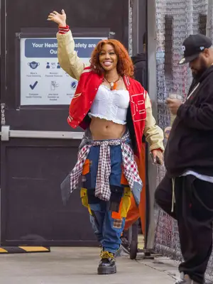 SZA wearing a red and white letterman jacket, a white cropped corset, patchwork pocket loose jeans, and a flannel tied around her waist. 