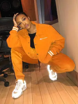 SZA wearing a matching orange track suit, white sneakers, and updo hairstyle