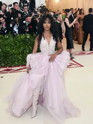 SZA wearing a light pink Versace gown with beaded bodice, beaded thigh-high stiletto boots, and a golden star headpiece to the 2018 Met Gala