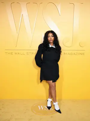SZA wears a black dress with white collar, white socks, and black heels 