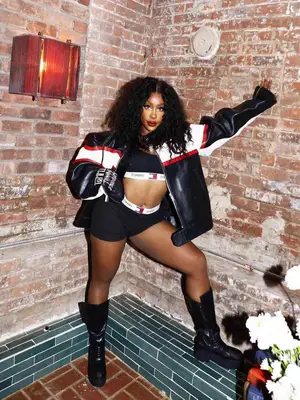 SZA in Tommy Hilfiger matching black underwear and an oversized black, red, and white leather jacket with black biker boots