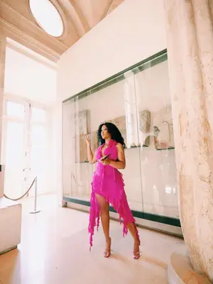 SZA wears a pink ruffled dress and open-toed heels while standing in a museum