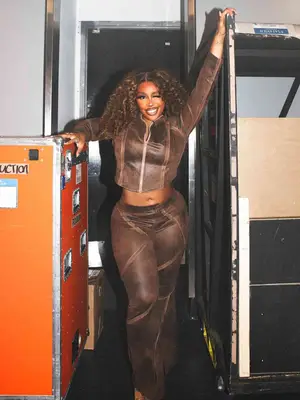SZA wearing a matching brown jacket and pants set while winking and posing backstage