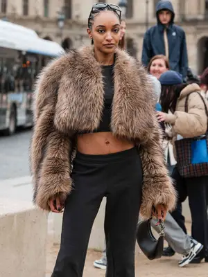 Model wearing a cropped fur jacket, black crop top and pants, and sunglasses on head
