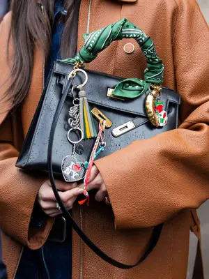 Close-up of person holding a handbag with multiple bag charms and green bandana