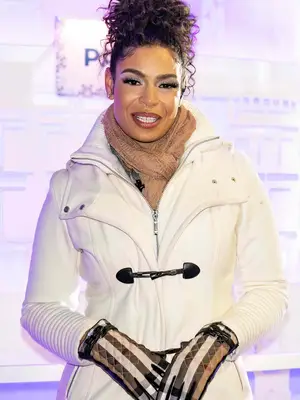 Jordin Sparks wearing a white toggle coat, tan looped scarf, and curly updo hairstyle