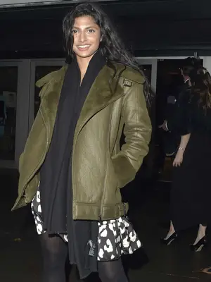 Priya Kansara wears a olive coat, long black scarf, black-and-white dress, and tights