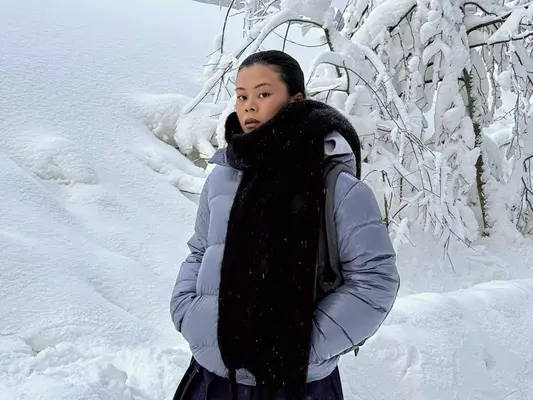 Woman wearing a cashmere scarf and puffer coat while standing in the snow