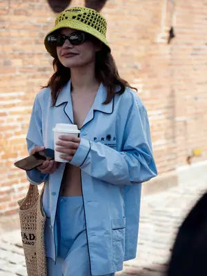 ea Nauman wearing light green bucket har, light blue Prada pants and matching light blue shirt with Prada logo with dandelion and brown big Prada bag posing outside OperaSpo during Copenhagen fashion week