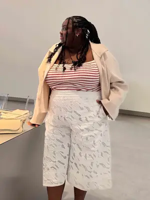 Abisola Omole wearing a red and white striped top, long lace shorts, and a cream jacket