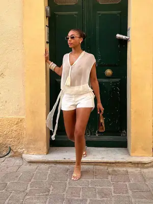 Lori Harvey wearing a cream top, white shorts, and gold sandals