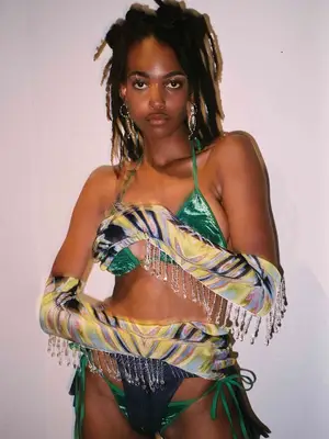 Model wearing green velvet bikini, patterned opera gloves with crystal drip, and dangling earrings