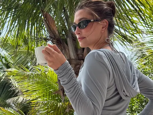 Hailey Bieber wearing a gray hoodie and sunglasses at the beach