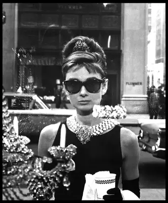 Audrey Hepburn in black dress, pearl necklace, updo with tiara, and black sunglasses