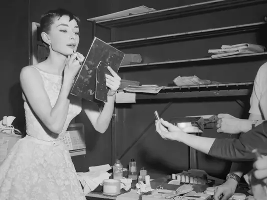 Audrey Hepburn applying lipstick in a handheld mirror
