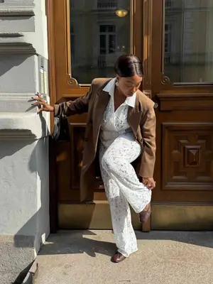 Nnenna Echem wears a white lace jumpsuit, brown tailored trench coat, brown flats, and black Dior handbag
