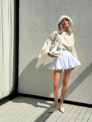Elsa Hosk wearing all-white outfit of crochet bucket hat, sweater, bubble tennis skirt, large handbag, and pointy kitten heels