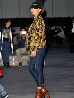Zendaya wearing graphic baseball cap, army print jacket, and skinny jeans