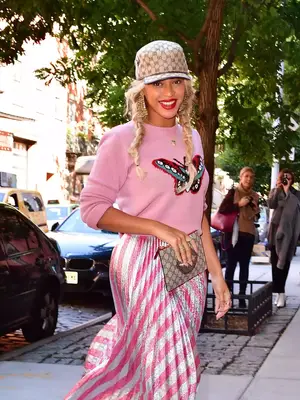 Beyonce wearing Gucci logo hat, pink sweater with butterfly, pink and silver skirt, and Gucci clutch