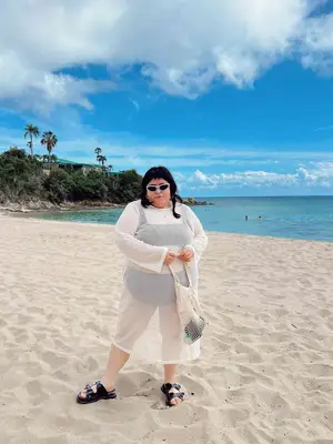 Jessica Torres wears a black bikini, a white sheer cover-up dress, white sunglasses, and black buckled sandals