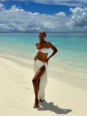 Jasmine Tookes wears a white bikini with a long white sarong and gold shell earrings