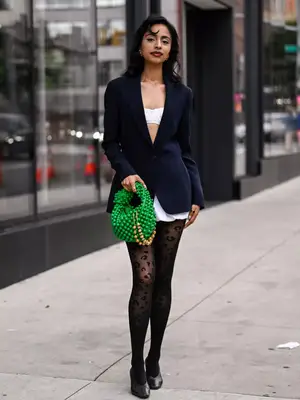 woman wearing a tailored navy blazer, white bralette top, short white skirt, and sheer animal print tights. 
