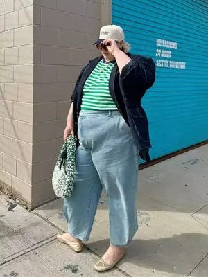 cAbby Bible wears a striped green shirt, black blazer, light-wash jeans, and trucker hat.