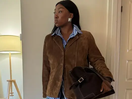 Nnenna Echem wears a brown suede blazer, blue and white striped shirt, and oversized handbag
