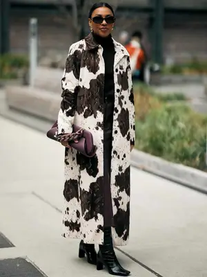 Morgan Evans wears a cow print longline coat, black outfit and boots, oxblood handbag, and sunglasses