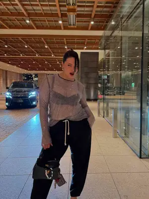 Ashley Graham wears a crystal mesh top, black bra, black drawstring sweatpants, and black handbag with bag charms