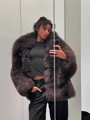 Imaan Hammam wears a gray t-shirt, black jeans, and voluminous brown furry coat