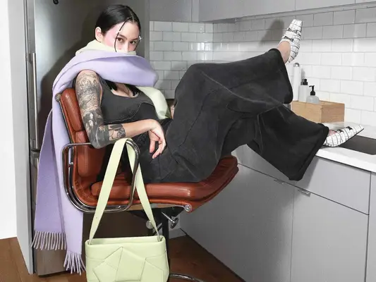 Michelle Zauner wears a gray leisurewear set, lavender scarf, light green handbag, and white croc bow mules