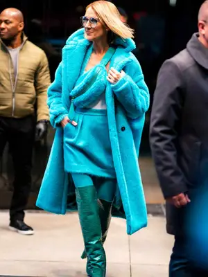 Celine Dion walking down the street in monochromatic blue outfit with fur coat and teal leather boots 