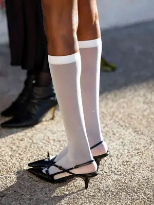 Close-up of person wearing black kitten heel slingback mules and knee-high sheer white stockings
