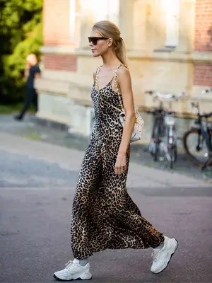 Woman wearing a cheetah print slip dress, shoulder bag, white sneakers, and sunglasses