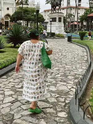 Woman wearing a printed dress, green tote, and green clogs