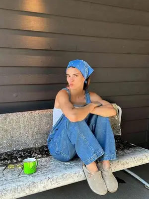 Kendall Jenner sitting on a bench and wearing overalls with clogs