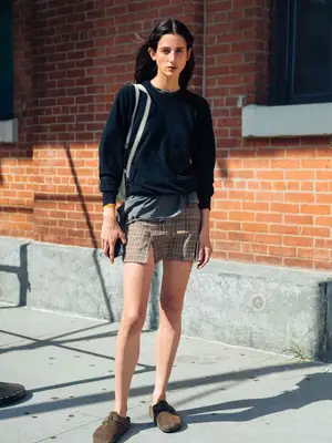 Person wearing a printed skirt, long sleeve sweater, and brown clogs