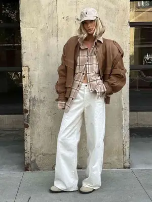Person posing while wearing white jeans, a jacket and plaid button-down top